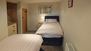 A bedroom with two single beds, a nightstand, a dresser, a mirror, and a radiator. - Grooms Cottage- Sleeps 4 in 2 bedrooms plus 2 to 4 dogs depending on size. (Bodmin)