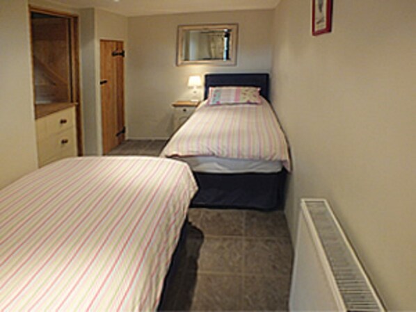 A bedroom with two single beds, a nightstand, a dresser, a mirror, and a radiator. - Grooms Cottage- Sleeps 4 in 2 bedrooms plus 2 to 4 dogs depending on size. (Bodmin)
