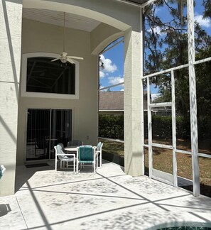 A covered outdoor patio with a table and chairs, a ceiling fan, and a view of the surrounding landscape.