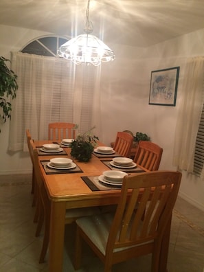 A dining room with a wooden table set for six, surrounded by six wooden chairs.