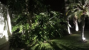 Ein Garten mit einem gepflegten Rasen, verschiedenen Bäumen und einer kleinen, beleuchteten Skulptur.