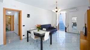 A modern living room with a dining table, sofa, and a balcony with a view. - Moressas two units accommodates up to 9 (Praiano)