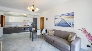 A modern kitchen with grey cabinets and white countertops, a dining area with a grey sofa and white chairs, and a large painting of a bridge on the wall. - Moressas two units accommodates up to 9 (Praiano)