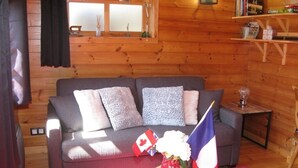 A cozy log cabin interior with a grey sofa, a small wooden table with a vase of flowers, and two flags on the table.