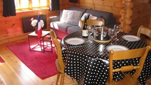 A cozy cabin interior with a dining table set for four, a sofa, and a window with curtains.