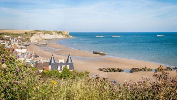 A coastal town with a sandy beach, a cliff, and a small harbor with boats.