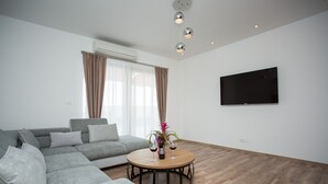 Una sala de estar moderna con un sofá seccional gris, una mesa de centro redonda y un televisor de pantalla plana montado en la pared.