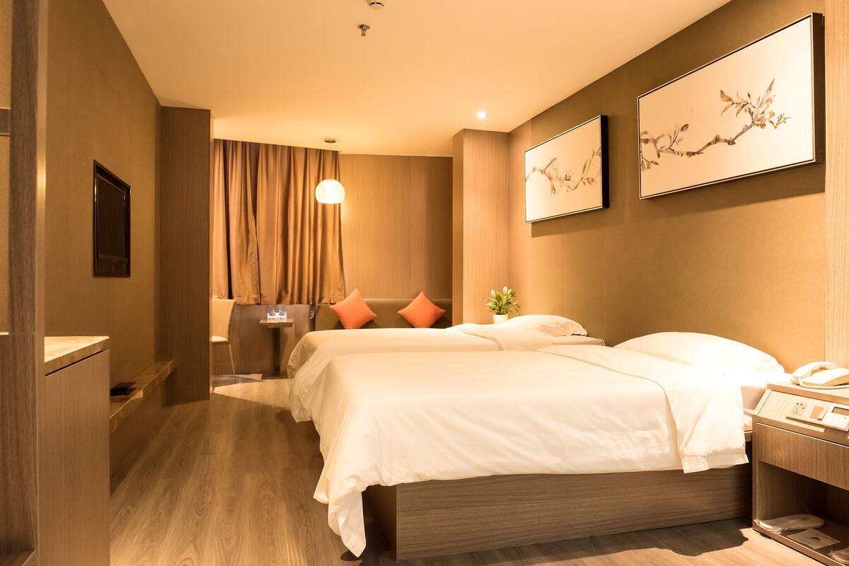 A hotel room with two beds, a bedside table, a lamp, and artwork on the wall.