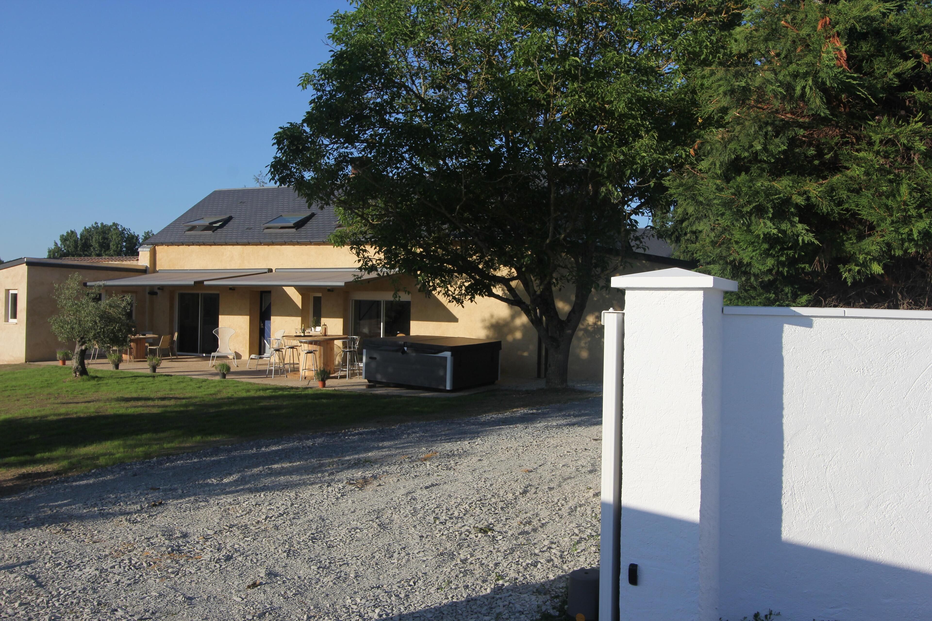A house with a gravel driveway, a patio area, and a large tree in front.