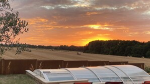 Ein Gewächshaus mit Glasdach, vier rote Stühle und Blick auf ein Feld und einen Sonnenuntergang.