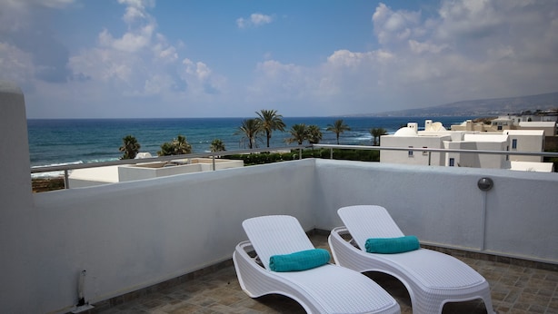 A balcony with two white lounge chairs, one with a teal cushion, overlooking a coastal area with palm trees and buildings. - NEW! Luxury 8 bed villa with magnificent roof terrace, 100m from the sea. (Chloraka)