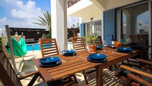 An outdoor dining area with wooden tables and chairs, blue plates, and wine glasses. - NEW! Luxury 8 bed villa with magnificent roof terrace, 100m from the sea. (Chloraka)