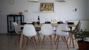 A dining area with a wooden table, white chairs, a black cabinet, a clock, a framed painting, and a potted plant. - NEW! Luxury 8 bed villa with magnificent roof terrace, 100m from the sea. (Chloraka)