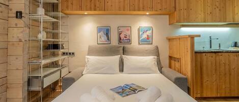 Una habitación de hotel con cama, pared de madera, estantería metálica y una pequeña kitchenette.
