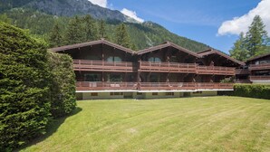 Ein Chalet-Stil-Gebäude mit mehreren Balkonen, einem gepflegten Rasen und einer Bergkulisse.
