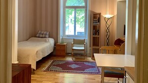 Ein Schlafzimmer mit Bett, Stuhl, Tisch, Bücherregal und einem Fenster mit Blick auf Bäume.