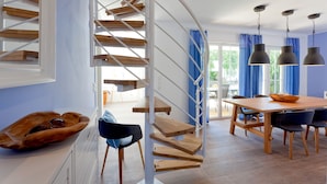 Een modern interieur met een houten trap, een eethoek met tafel en stoelen, en hanglampen.