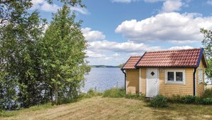 Una petita cabana de fusta amb teules vermelles, a la vora d'un llac sota un cel blau i vegetació abundant.