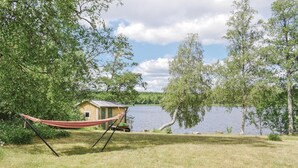 Una cadira de fil a una zona enjardinada, amb una petita cabana de fusta al costat d'un llac.