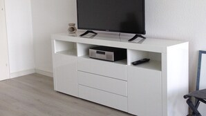 A white entertainment unit with a flat-screen TV, a DVD player, and a remote control. - Apartment with a dream view directly on the Pearl Bay (Büsum)