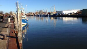 A harbor with several boats docked, a pier with people walking, and a building in the background. - Apartment with a dream view directly on the Pearl Bay (Büsum)