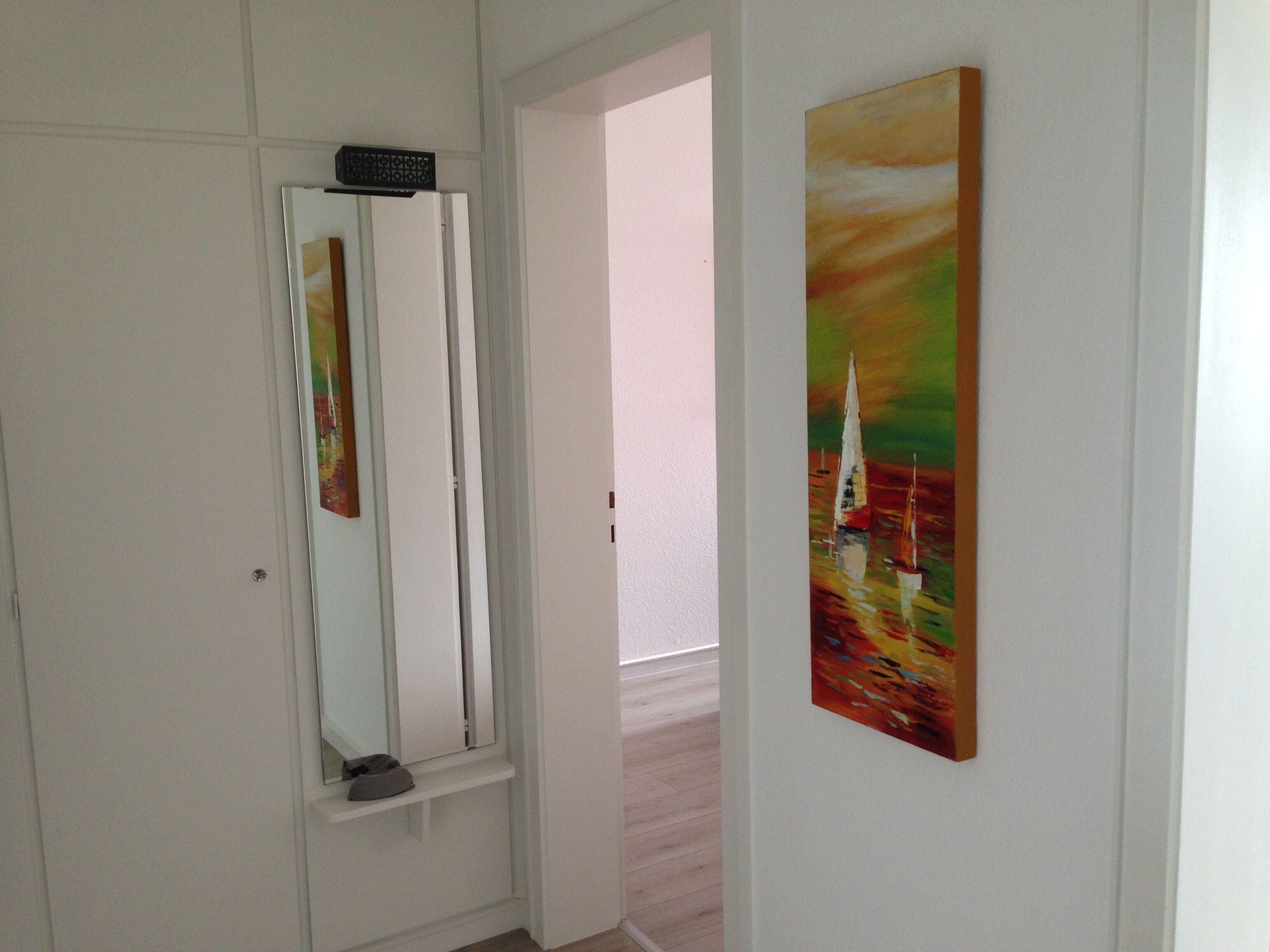 A hallway with a white door, a mirror, and a painting of sailboats.