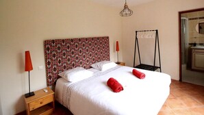 A neatly made bed with white linens and red towels, a patterned headboard, a bedside table with a lamp, and a hanging light fixture.