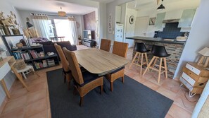 A modern living room with a dining table, wicker chairs, a bookshelf, and a television.