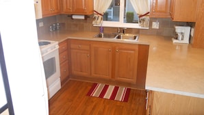 A kitchen with wooden cabinets, a built-in oven, a sink, and a window with curtains. - Cozy country bungalow within the Amish Community (Leacock-Leola-Bareville)