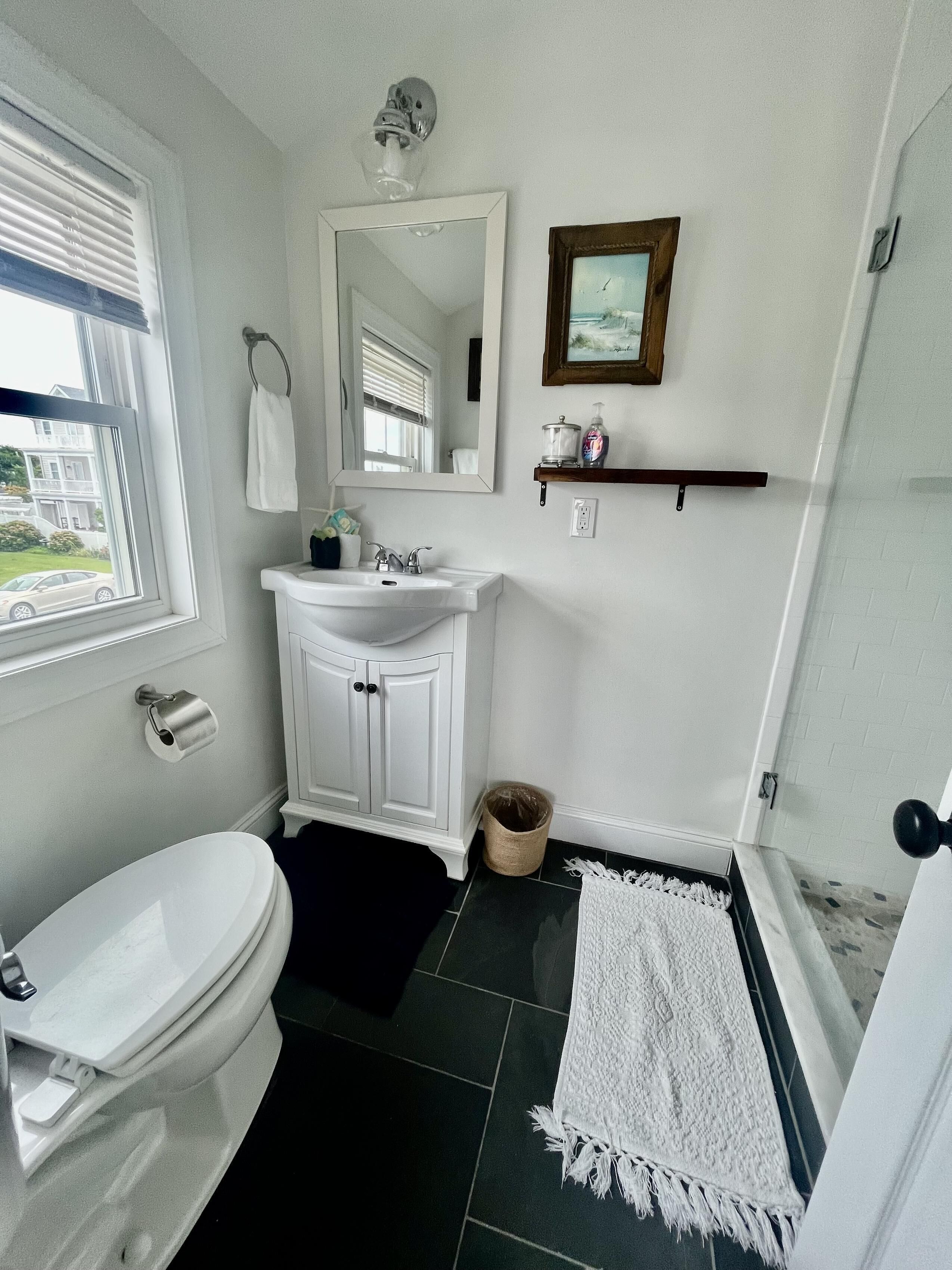 A bathroom with a toilet, sink, mirror, and shower area.