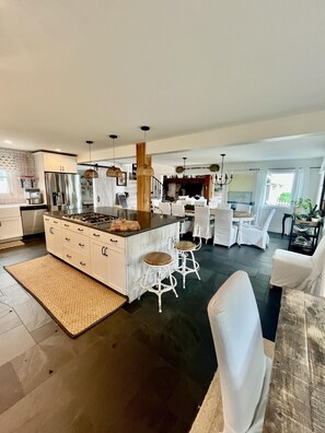 A modern kitchen with a central island, white bar stools, and a dining area with white chairs. - Renovated, Amazing Bayview Sunsets, 5 Bd/4 Bath, Sleeps 14. Multifamily Getaway (Brigantine)