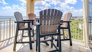 Ein Balkon mit drei Adirondack-Stühlen und einem Tisch, mit Blick auf einen Strand und den Ozean.