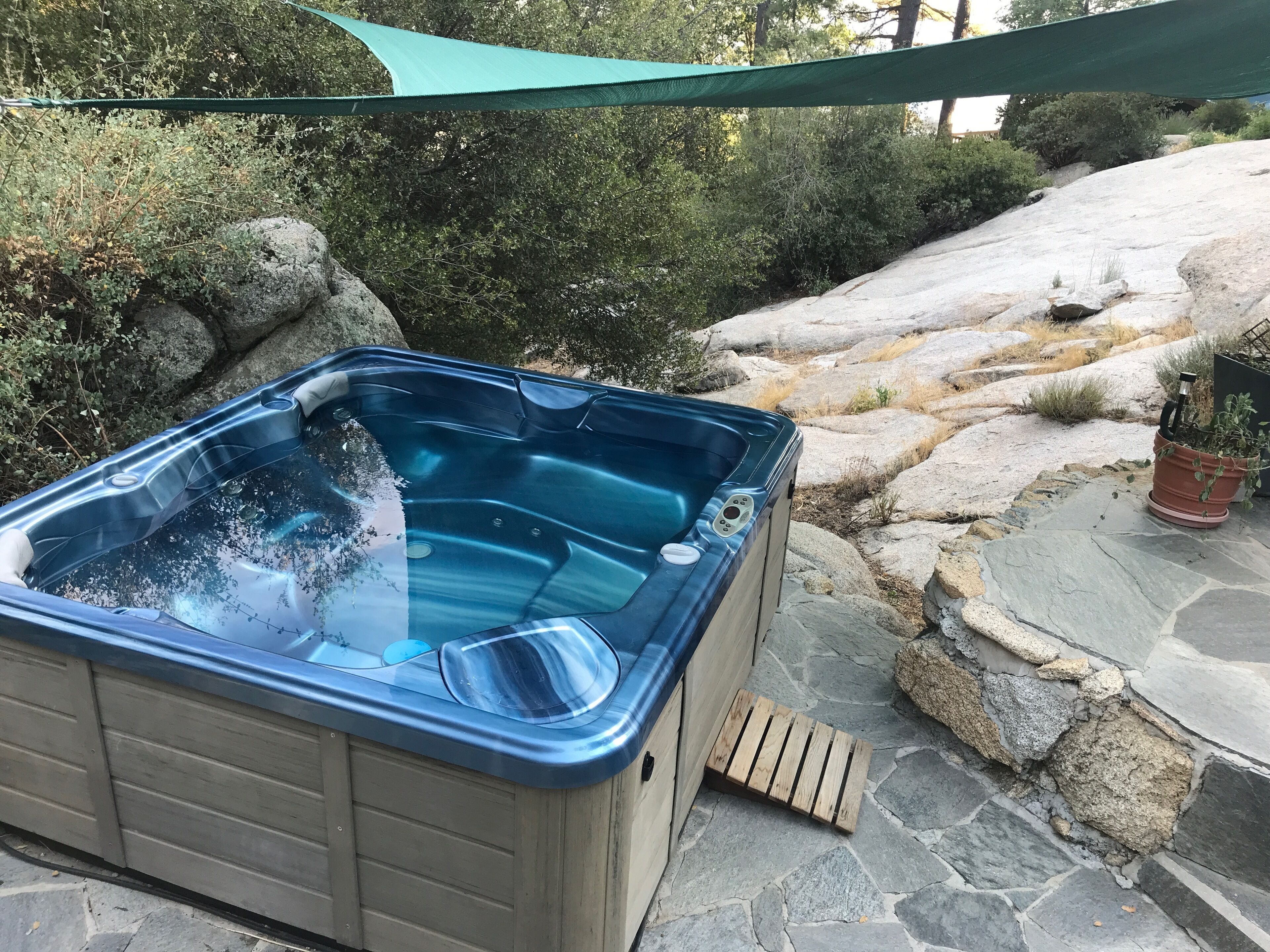 A hot tub with a wooden footrest and a stone pathway.