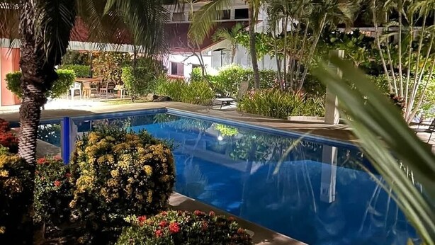 Ein Pool, umgeben von üppiger Vegetation und Palmen, mit einem Gebäude im Hintergrund.