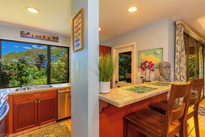 Una cocina con un ventanal grande, un comedor con mesa y sillas, y vistas a zonas verdes exteriores.