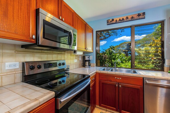 Una cocina moderna con electrodomésticos de acero inoxidable, armarios de madera y un amplio ventanal con vistas a la vegetación.