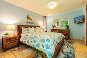 Un dormitorio con cama, mesitas de noche, cómoda, espejo y televisión.