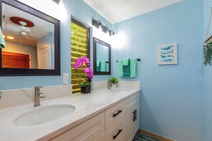 A bathroom with two sinks, a mirror, a ceiling fan, and a wall-mounted light fixture.