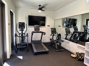 Un gimnasio en casa con cintas de correr, elípticas y una bicicleta estática, equipado con monitores de actividad física.