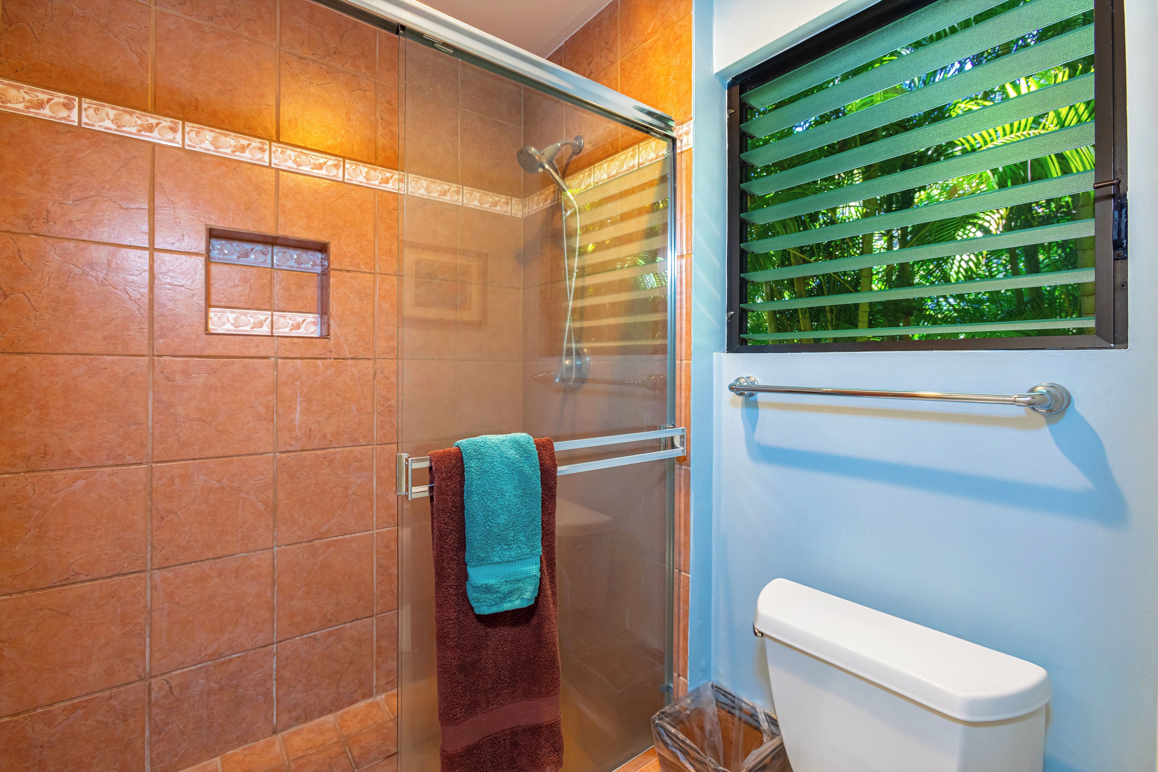 A bathroom with a shower, a toilet, and a window with blinds.