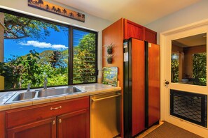 A kitchen with a large window, wooden cabinets, a stainless steel sink, and a refrigerator.