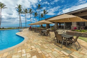 Un área junto a la piscina con una piscina curvada, mobiliario exterior, palmeras y vistas al océano.