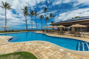A swimming pool with palm trees and lounge chairs, surrounded by a covered patio area.