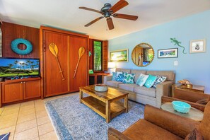 A living room with a wooden ceiling fan, a television, a sofa with patterned cushions, and a coffee table.
