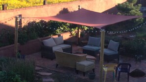 Une terrasse extérieure aménagée avec des meubles en osier, un auvent rouge et un espace jardin agrémenté de pas japonais et de plantes.