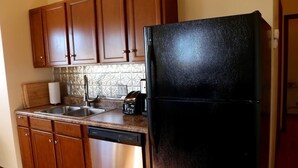 Une cuisine avec des meubles en bois, un lave-vaisselle en acier inoxydable, un réfrigérateur noir et un dosseret carrelé.