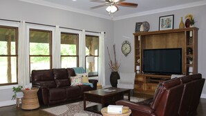 A living room with a brown leather sofa, a coffee table, a TV, and a wooden entertainment center. - Private 36-Acre Ranch Near Austin & Dripping Springs - Pond & Fire Pit (Driftwood)