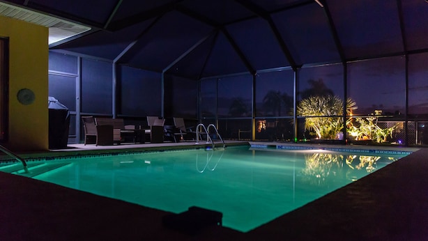 Een zwembad met een overdekt gedeelte, stoelen en uitzicht op de omgeving bij nacht.