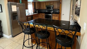 Een moderne keuken met een centraal eiland, barstoelen, een koelkast, magnetron en een spoelbak.