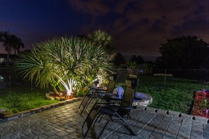 Relax in a serene outdoor space with a table and chairs, surrounded by lush greenery and a majestic palm tree.